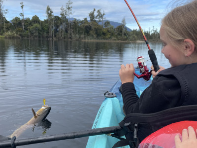 Kyah Sutherland brings a trout to the kayak in Lake Brunner.